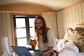 Happy young man with coffee and laptop in bed