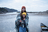 Happy young couple wrapped in a blanket on beach