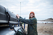 Smiling young man fastening canoe onto car at beach