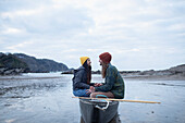 Happy young couple sitting in canoe on wet beach