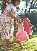 Happy mother and daughter dancing in sunny backyard