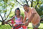 Happy grandfather and granddaughter riding bike in park