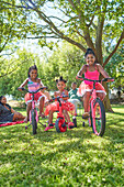 Sisters riding bicycles and tricycle in park
