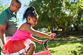 Father helping daughter learn to ride bike in sunny park