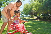 Grandfather pushing granddaughter on tricycle in park