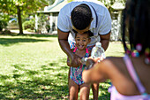 Father and daughters playing with water squirt bottles
