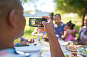Man with smartphone photographing family at patio table