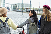 Young female friends with bicycle on urban sidewalk