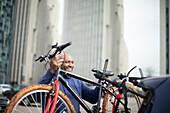 Happy man lifting bicycle onto car rack in city