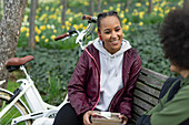 Happy young woman eating lunch with friend on park bench