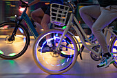 Men riding illuminated bicycles on sidewalk at night