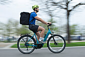 Male courier riding bicycle with delivery bag on sidewalk