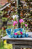 Posies of freesias and chamomile flowers in glass vases, bird figurines and blue egg carton