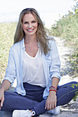 Long-haired woman in spring-like blue and white outfit sitting on the beach