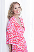 Long haired woman in pink patterned dress sitting on the beach