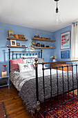 Metallbett mit Wandregalen in blauem Schlafzimmer und Holzfußboden