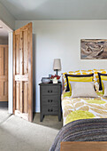 Bedroom with yellow bed linen, bedside table and rustic wooden door