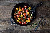 Mixed varieties of tomatoes in a skillet with thyme, rosemary, garlic cloves, bay leaves