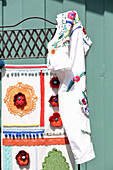 Paravent mit Spitzendecken, Borten, Häkelblüten und Pompons, besticktes Kleid aufgehängt
