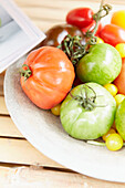 Different colored tomatoes on a plate, wooden background