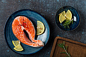 Raw fresh fish salmon steak top view on plate rustic dark concrete stone background with rosemary, lemon wedges and spices