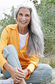 Reife Frau mit grauen Haaren in orangefarbener Bluse und Hose am Strand