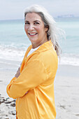Mature woman with grey hair in orange blouse sitting on the beach