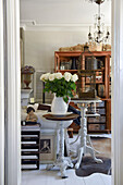 White roses in jug vase on round side table in living room with antique furniture