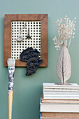 DIY picture frame with wicker rack holding various mementos, stack of books, paintbrush and vase with dried plants