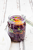 Jar of red cabbage, chili peppers, carrots and coriander on wooden table