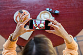 Draufsicht einer Frau in einem Café, die ein Handyfoto macht