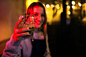 Lächelnde junge Frau, die nachts ein Getränk zeigt
