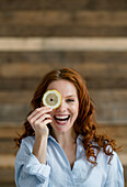 Porträt einer lachenden rothaarigen Frau, die das Auge mit einer Zitronenscheibe bedeckt