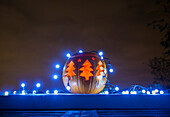 Jack o lantern decorated with blue Christmas lights glowing outdoors at night