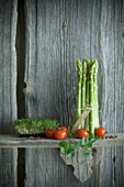 Bundle of green asparagus, tomato, cress, parsley and mixed pepper on wood
