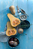 Whole and sliced butternut squash, garlic cloves and herbs on light blue wood