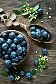 Bowl of blueberries, wooden spoon, blueberry blossoms on wood