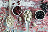Various beans in spoons and bowl on table