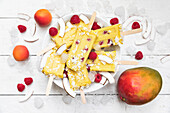 Homemade mango and apricot popsicles with raspberries and coconut chips
