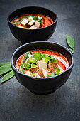 Bowls of red Thai Curry with snow peas, carrots, bell pepper, spring onions and smoked tofu