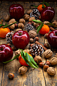 Rote Äpfel, Mandarinen, Haselnüsse, Walnüsse, Zimtstangen und Tannenzapfen auf dunklem Holz
