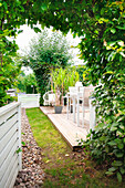 Holzterrasse mit Pflanzkübeln und Gartenmöbeln umgeben von Grün