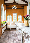 Dining and seating area in the orangery with partially arched windows and ochre-colored walls