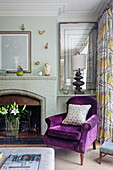 Living room with purple armchair, fireplace and patterned curtains