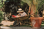 Mother holding daughter sitting in wheelbarrow at yard