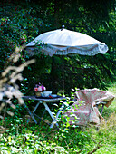 Garden chair with flowered blanket and table under a fringed parasol