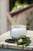 Homemade bath salts in a glass jar with rose blossoms, rosemary, juniper berries