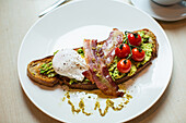 Toasted bread with avocado, bacon, poached egg and tomatoes