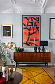 Sideboard mit Dekoobjekten, darüber moderne Kunst im Wohnzimer mit Stuckdecke