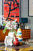 Runder Couchtisch mit Vasen, dahinter Sideboard und moderne Kunst im Wohnzimmer